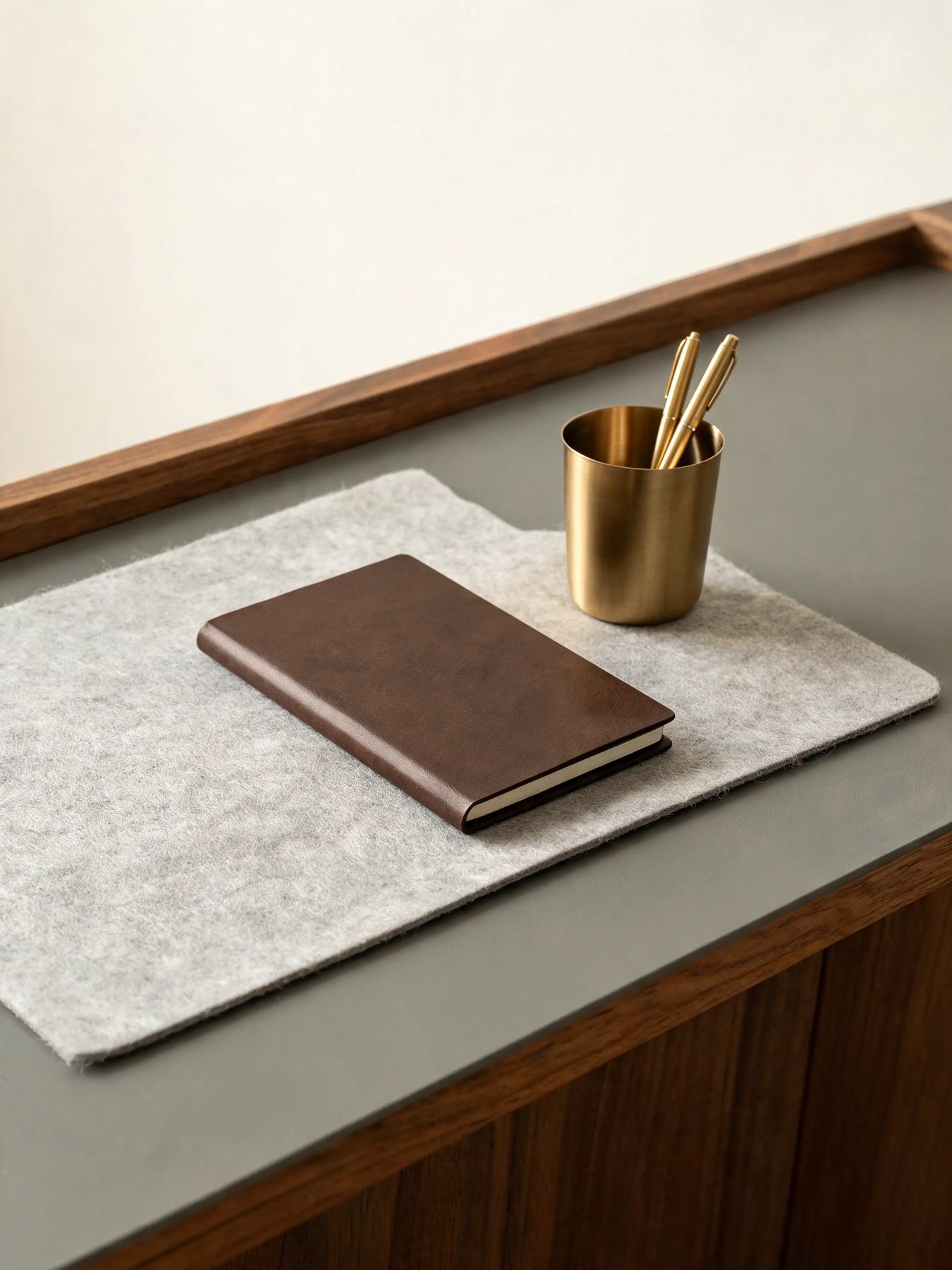 Walnut desk shelf with a felt mat and a brass pen cup on a matte grey desk